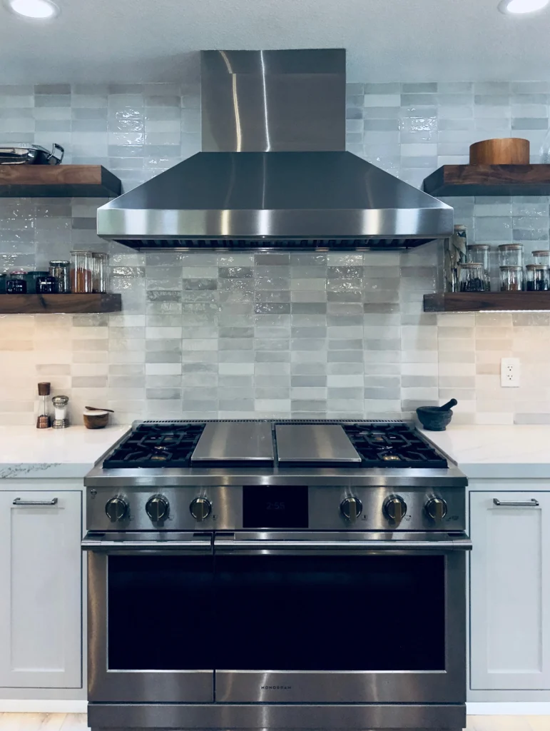 Warm modern kitchen remodel featuring handcrafted zellige-style backsplash tiles behind professional stainless range and statement hood in Granite Bay, CA by Tenax Construction